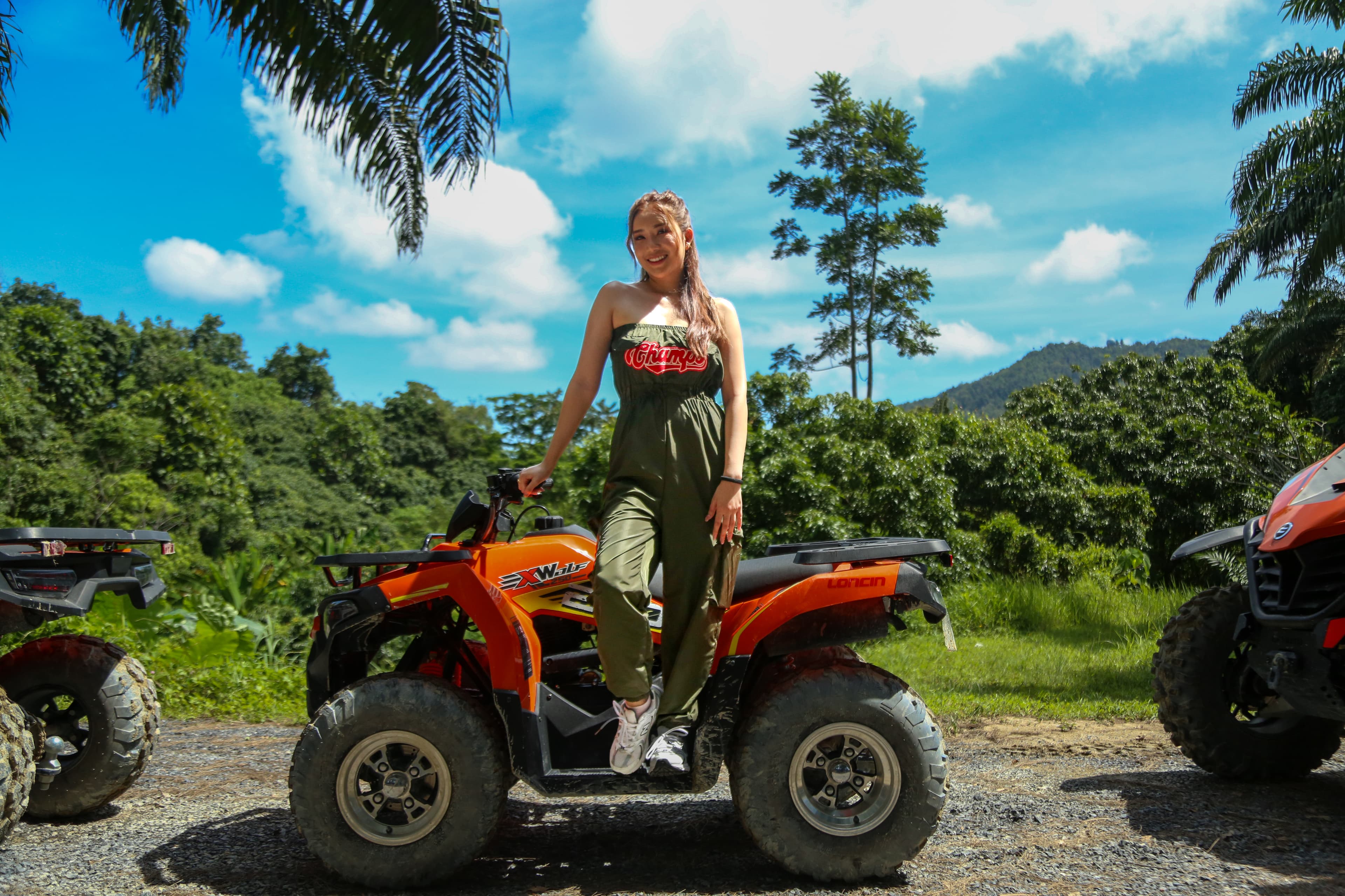 Guest standing on an orange ATV with jungle and blue sky behind